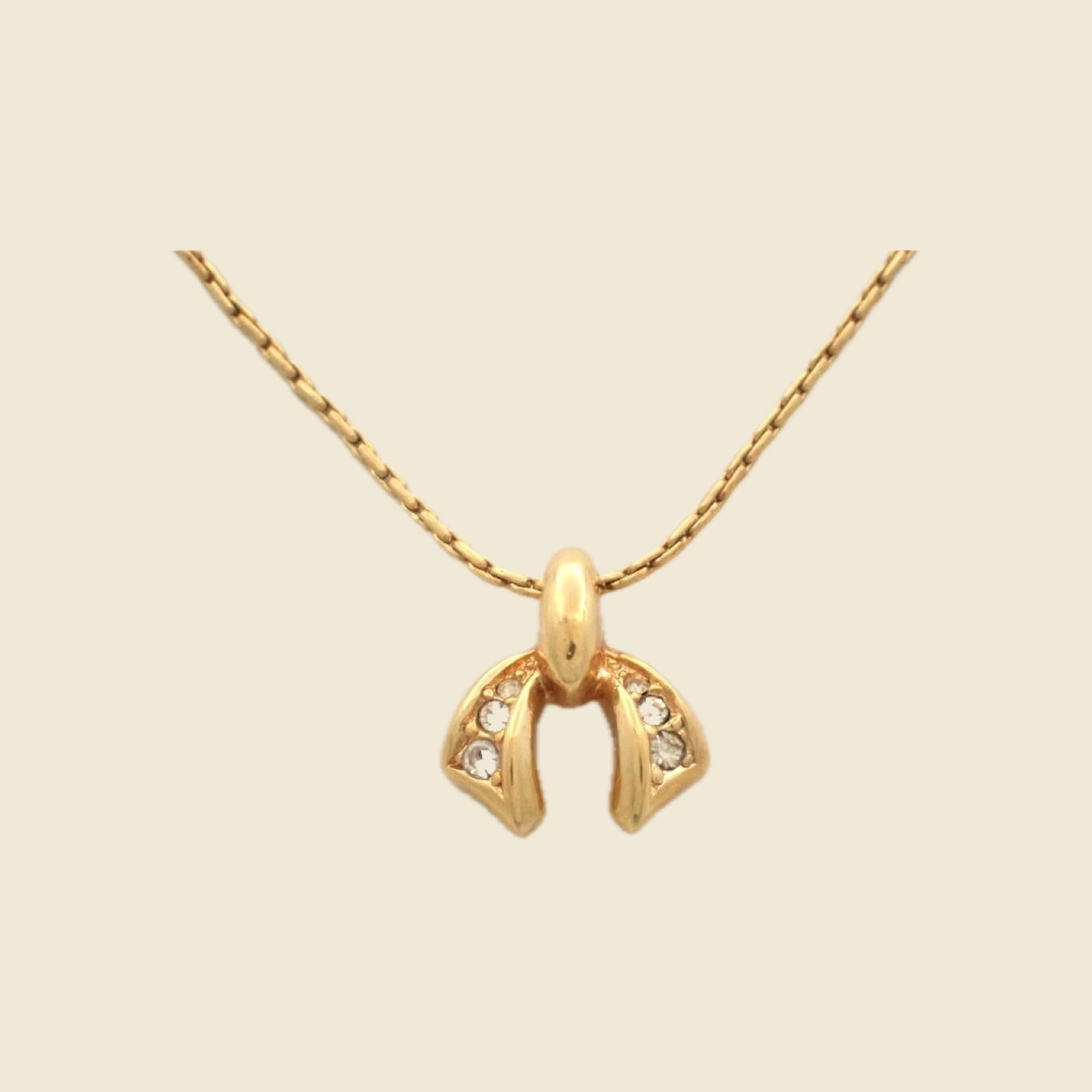 Collana Christian Dior in metallo dorato con pendente arcuato a pietre chiare e catena sottile, su fondo neutro