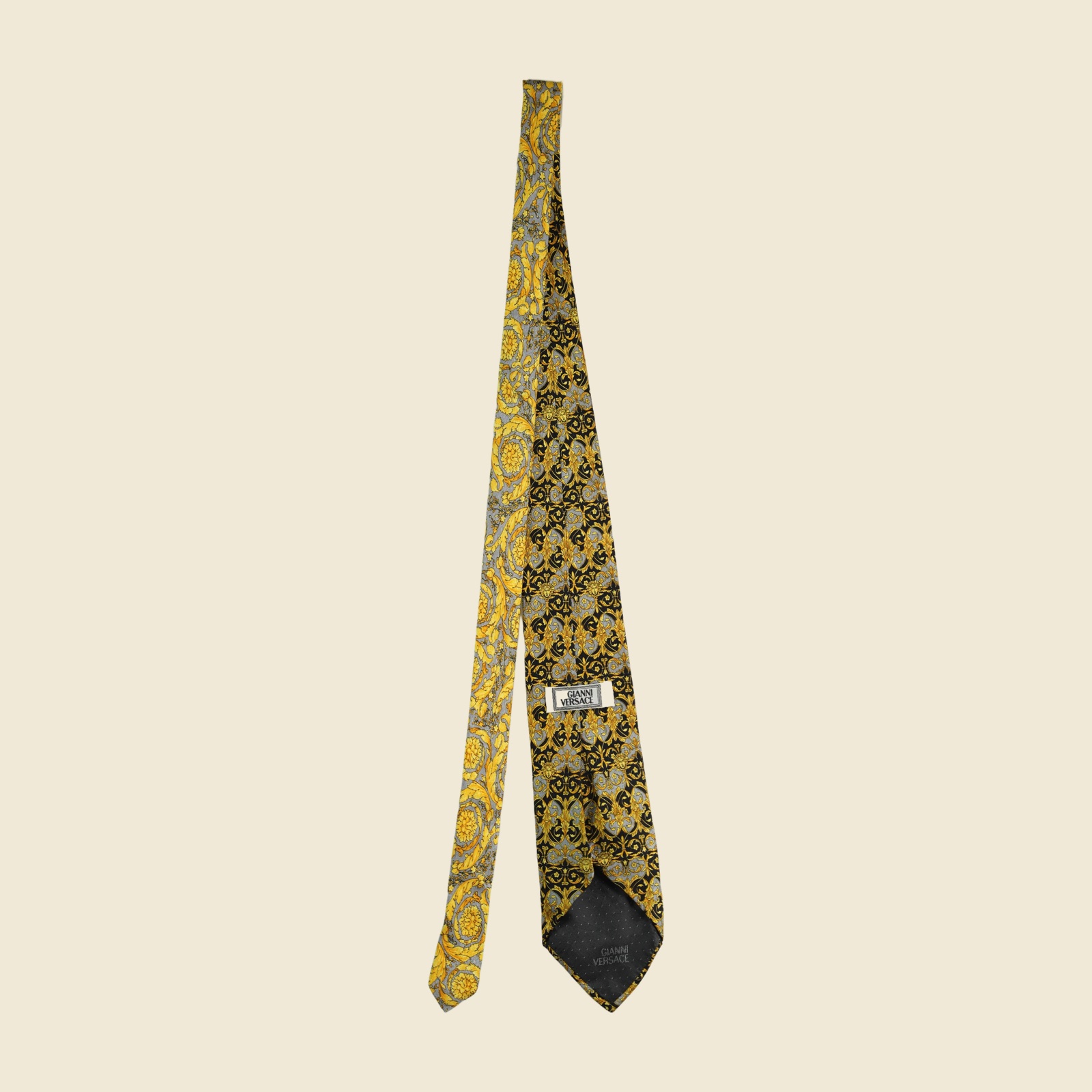 Cravatta Gianni Versace barocca a pannello, volute e mascheroni in oro su fondo nero e grigio argento, vista frontale su fondo neutro
