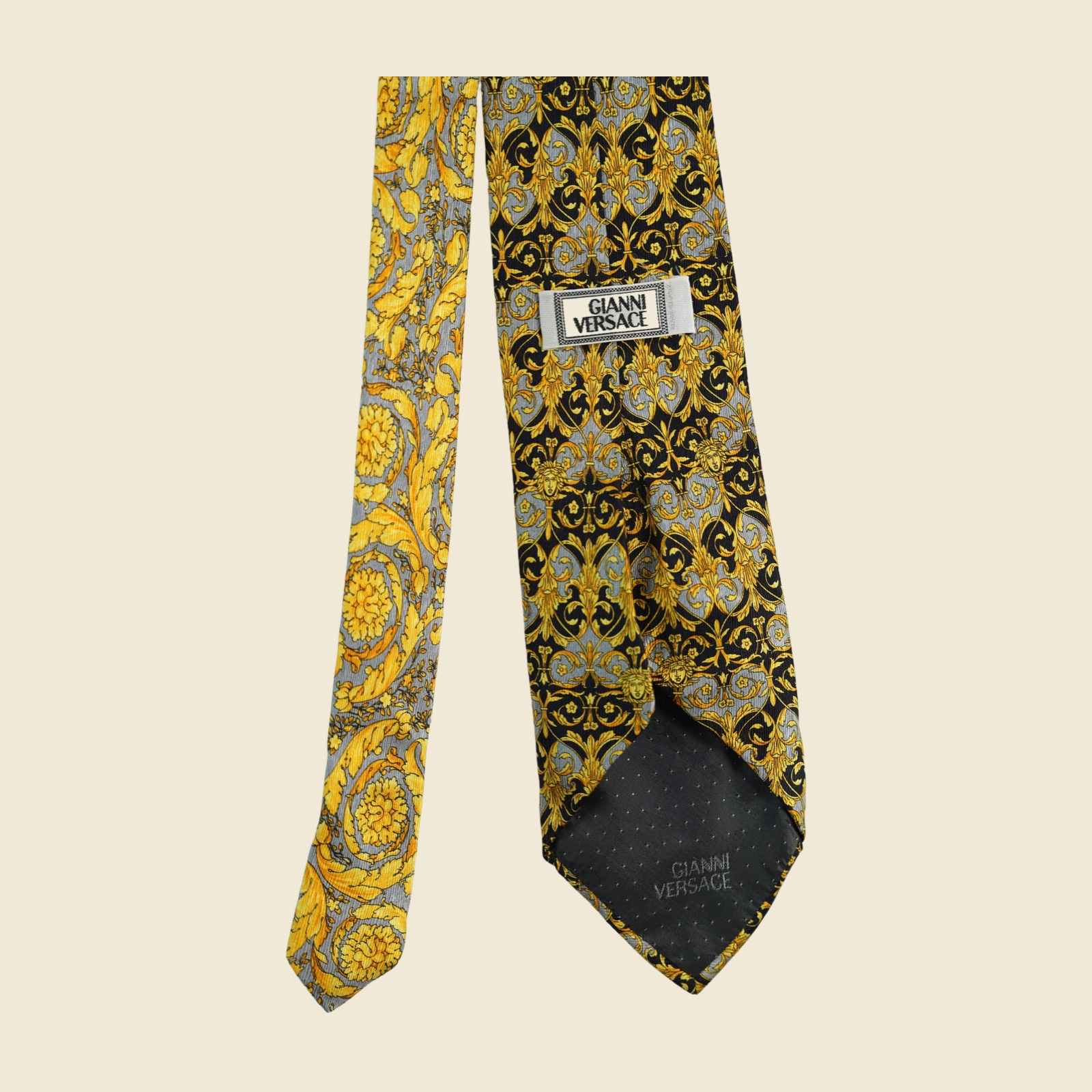 Cravatta Gianni Versace barocca a pannello, volute e mascheroni in oro su fondo nero e grigio argento, vista frontale su fondo neutro — vista 2