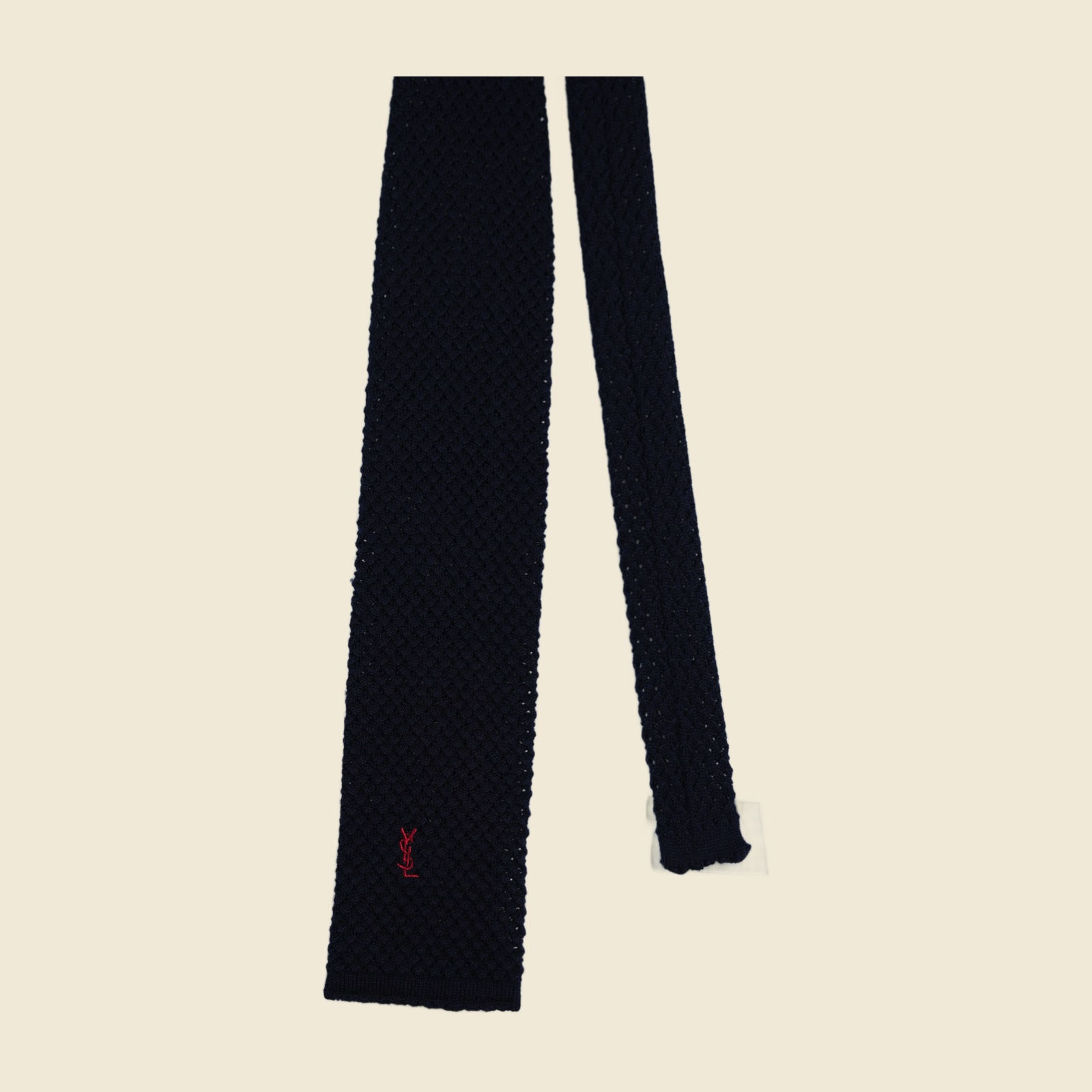 Cravatta Yves Saint Laurent in maglia blu notte a punta quadra, con monogramma YSL ricamato rosso sul lembo largo, distesa su fondo bianco — vista 2