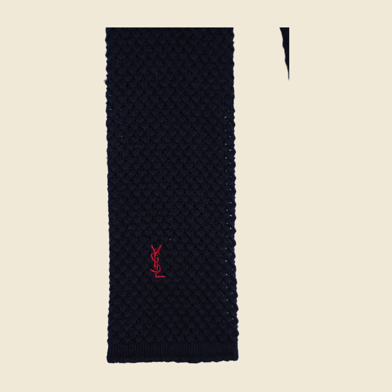 Cravatta Yves Saint Laurent in maglia blu notte a punta quadra, con monogramma YSL ricamato rosso sul lembo largo, distesa su fondo bianco — vista 3