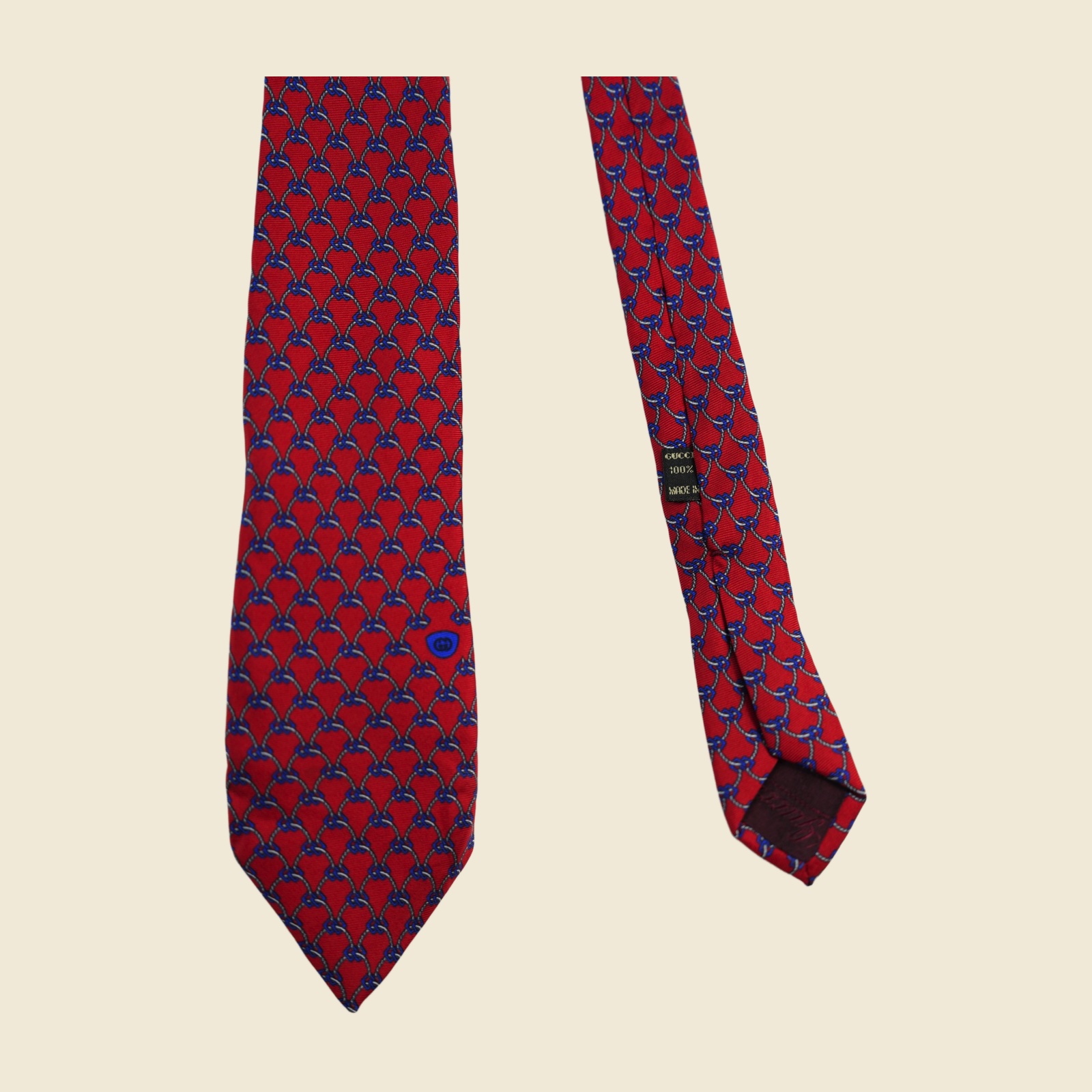Cravatta Gucci a reticolo di corde e catenelle annodate, grigio-argento e blu su fondo rosso, vista intera in posa piatta