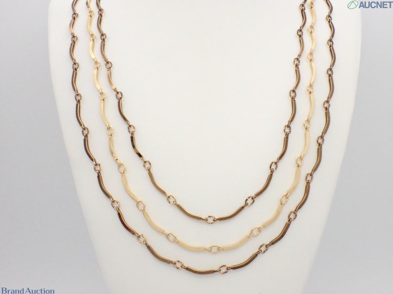 Collana Yves Saint Laurent a tre fili di barrette curve in metallo dorato, esposta su busto bianco su fondo neutro.