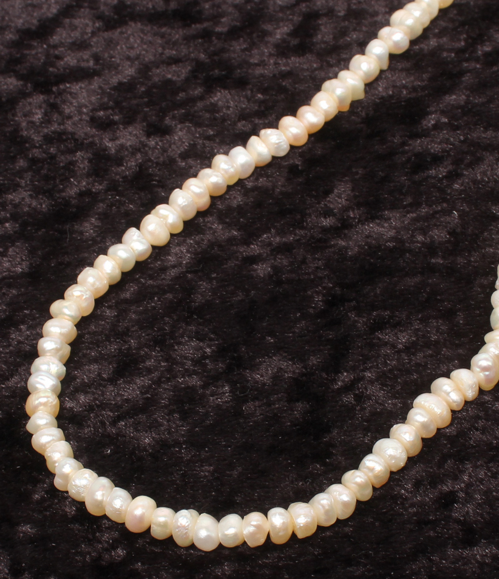 Collana a un filo di piccole perle d'acqua dolce irregolari, color avorio, adagiata su velluto scuro