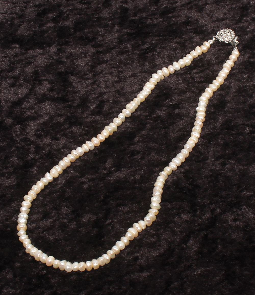Collana a un filo di piccole perle d'acqua dolce irregolari, color avorio, adagiata su velluto scuro — vista 2