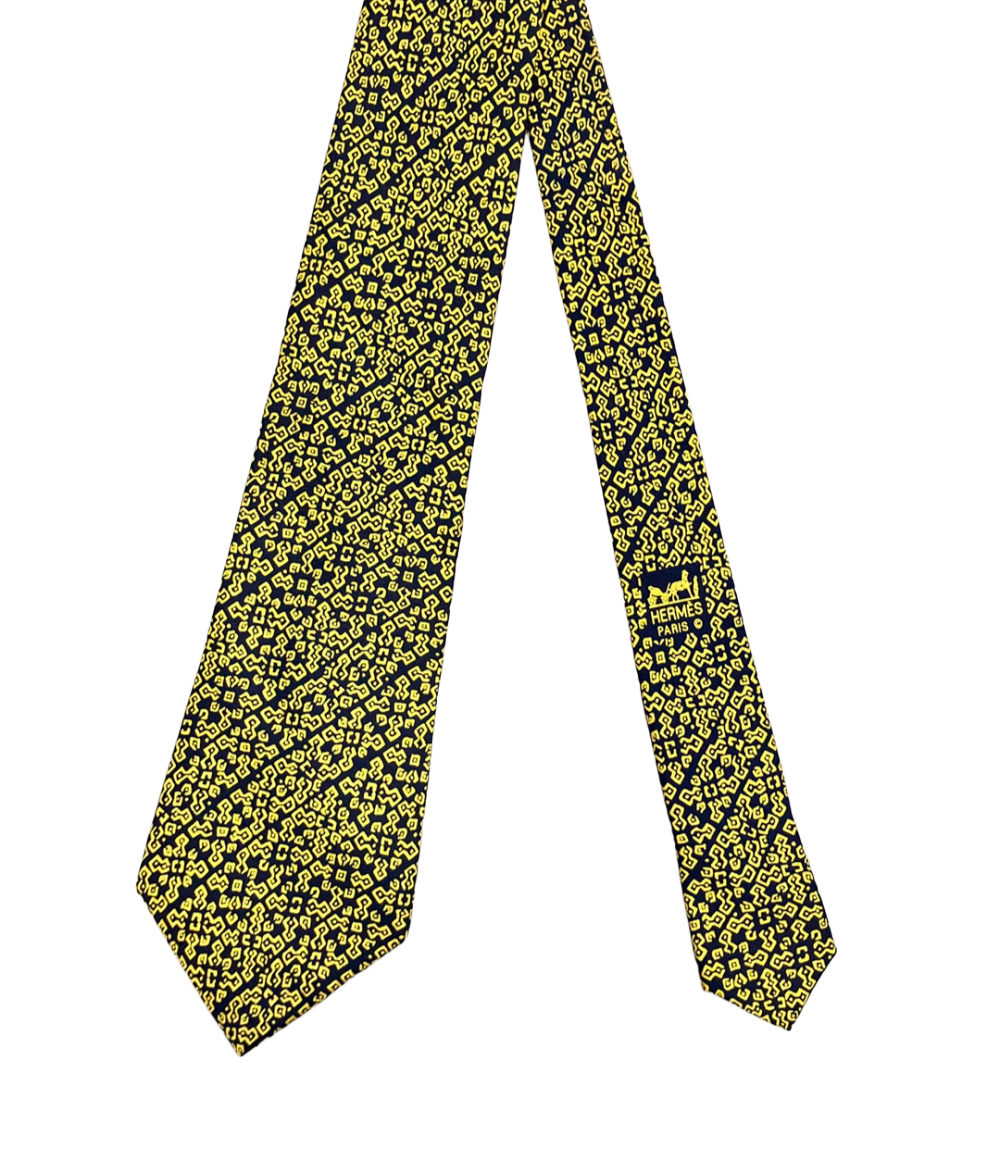 Cravatta Hermès in seta blu notte con motivo geometrico giallo a bande diagonali, ripiegata su fondo bianco — vista 2