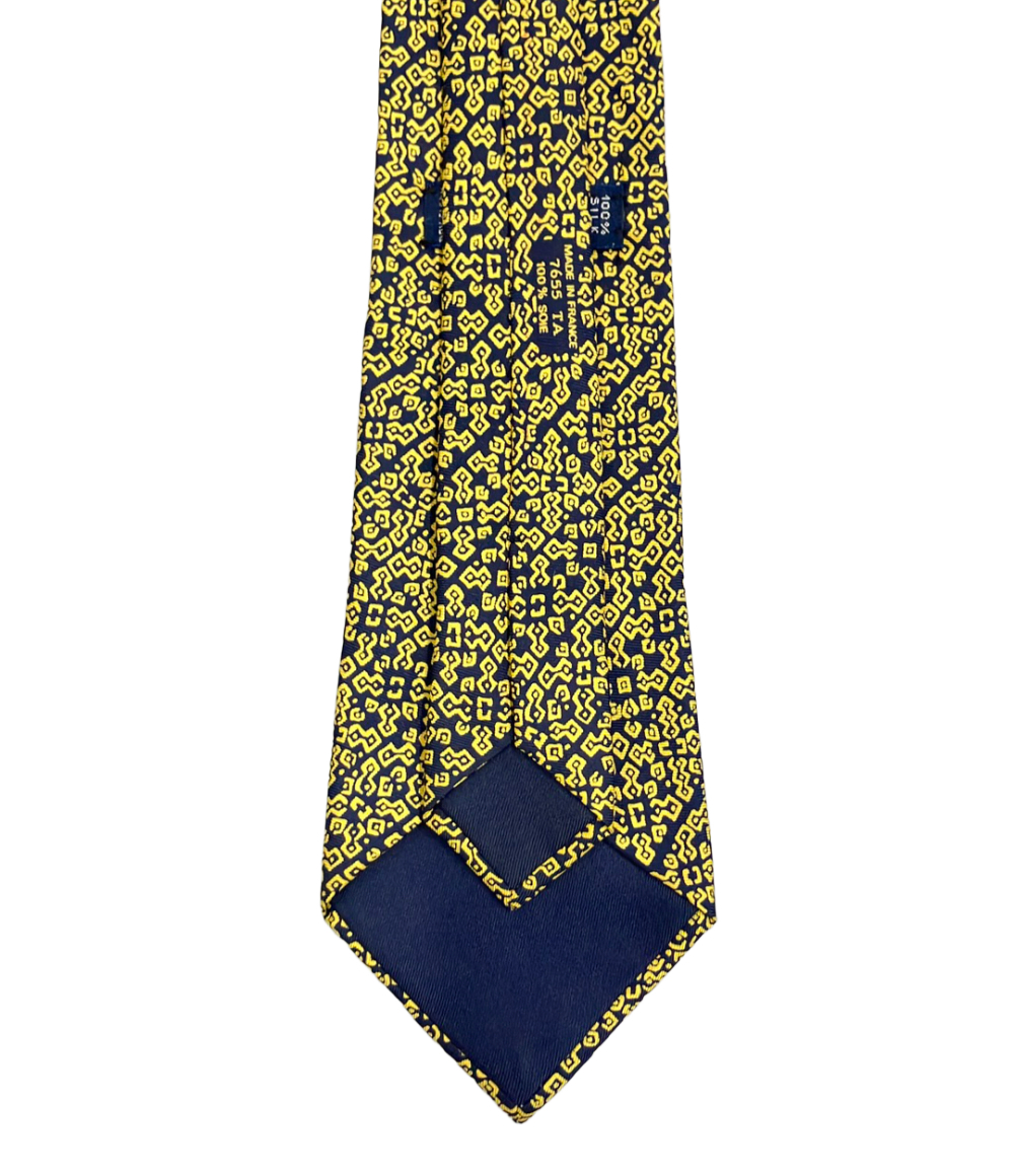 Cravatta Hermès in seta blu notte con motivo geometrico giallo a bande diagonali, ripiegata su fondo bianco — vista 3