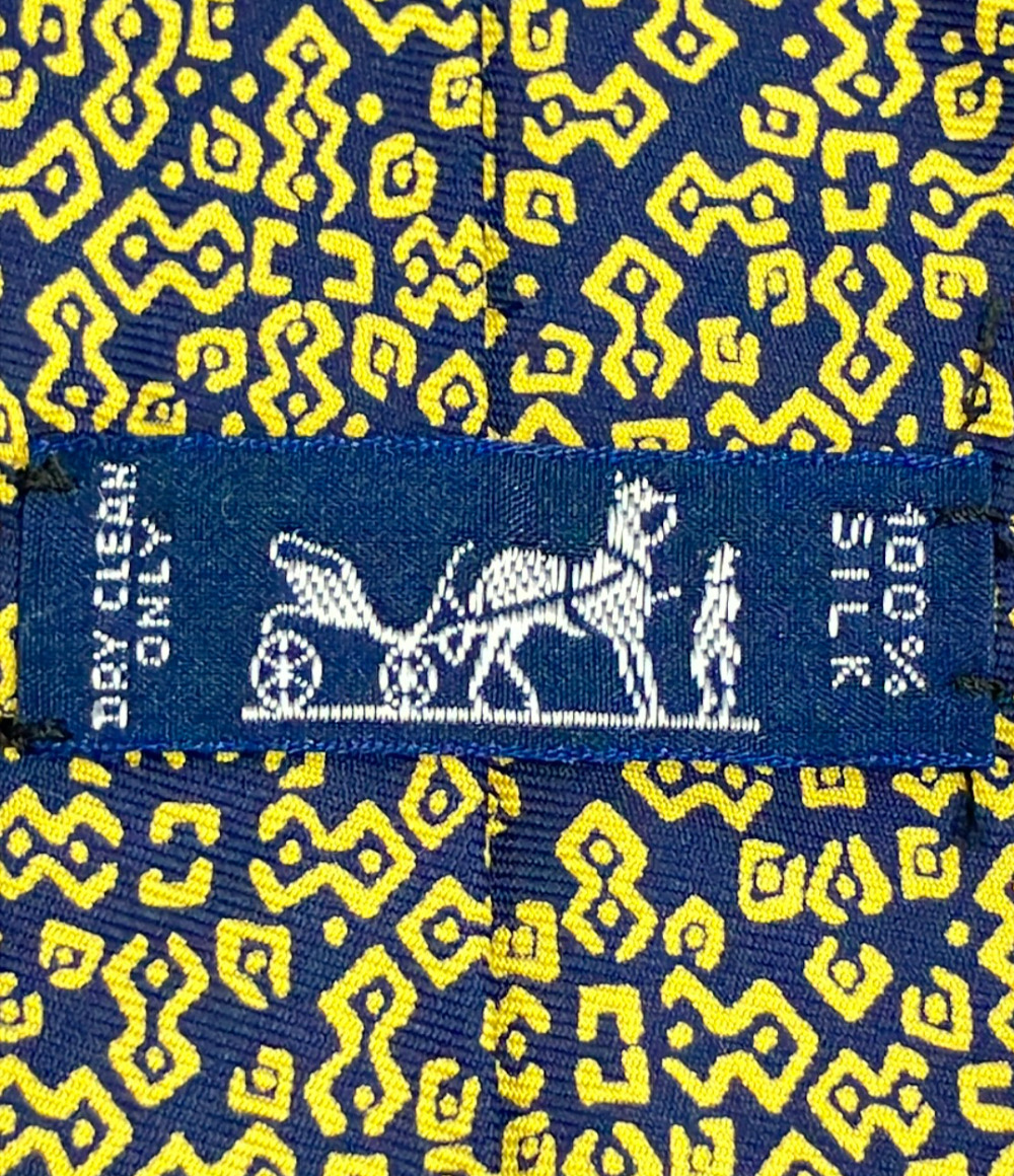 Cravatta Hermès in seta blu notte con motivo geometrico giallo a bande diagonali, ripiegata su fondo bianco — vista 4