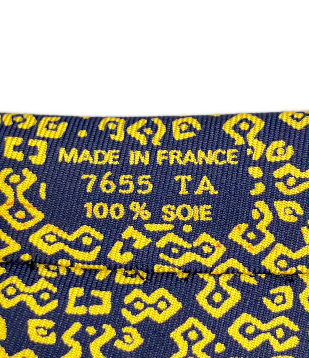 Cravatta Hermès in seta blu notte con motivo geometrico giallo a bande diagonali, ripiegata su fondo bianco — vista 5