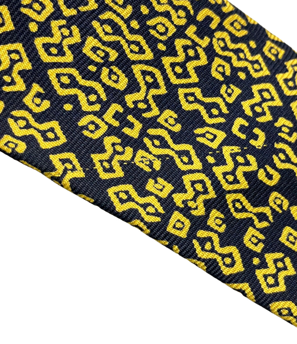 Cravatta Hermès in seta blu notte con motivo geometrico giallo a bande diagonali, ripiegata su fondo bianco — vista 6