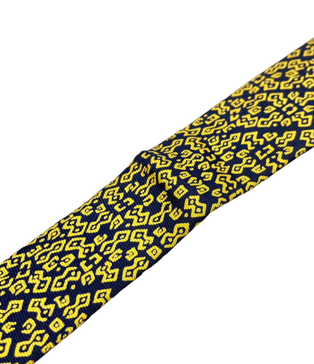 Cravatta Hermès in seta blu notte con motivo geometrico giallo a bande diagonali, ripiegata su fondo bianco — vista 7