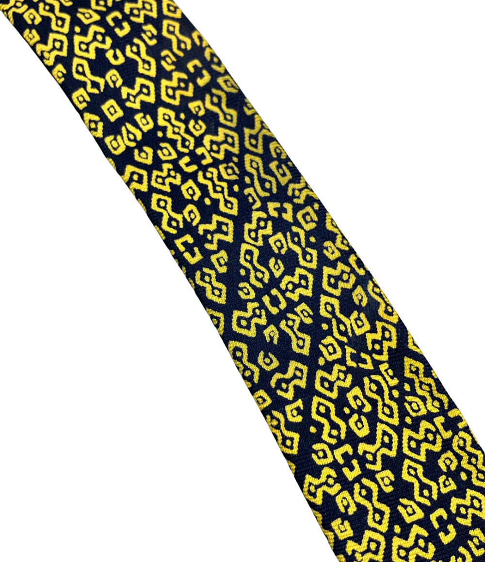 Cravatta Hermès in seta blu notte con motivo geometrico giallo a bande diagonali, ripiegata su fondo bianco   — vista 8