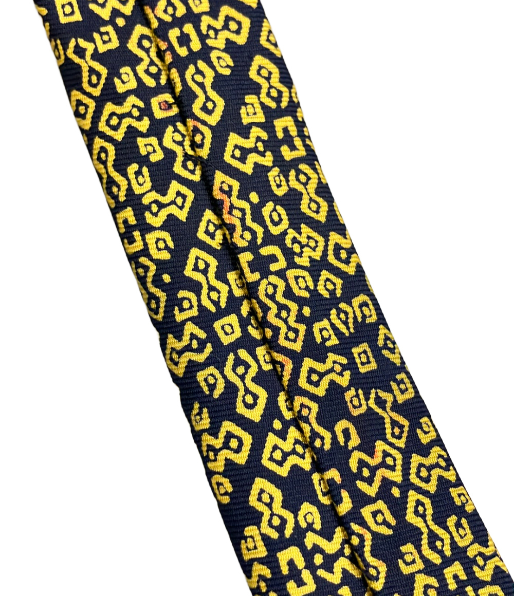 Cravatta Hermès in seta blu notte con motivo geometrico giallo a bande diagonali, ripiegata su fondo bianco — vista 9