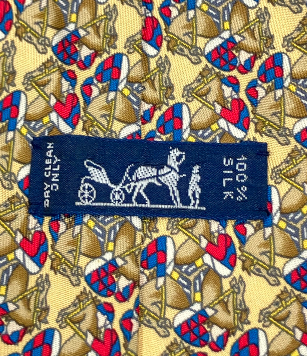 Cravatta Hermès in seta giallo paglia con cavalli e fantini in rosso e blu, ripiegata su fondo bianco — vista 4