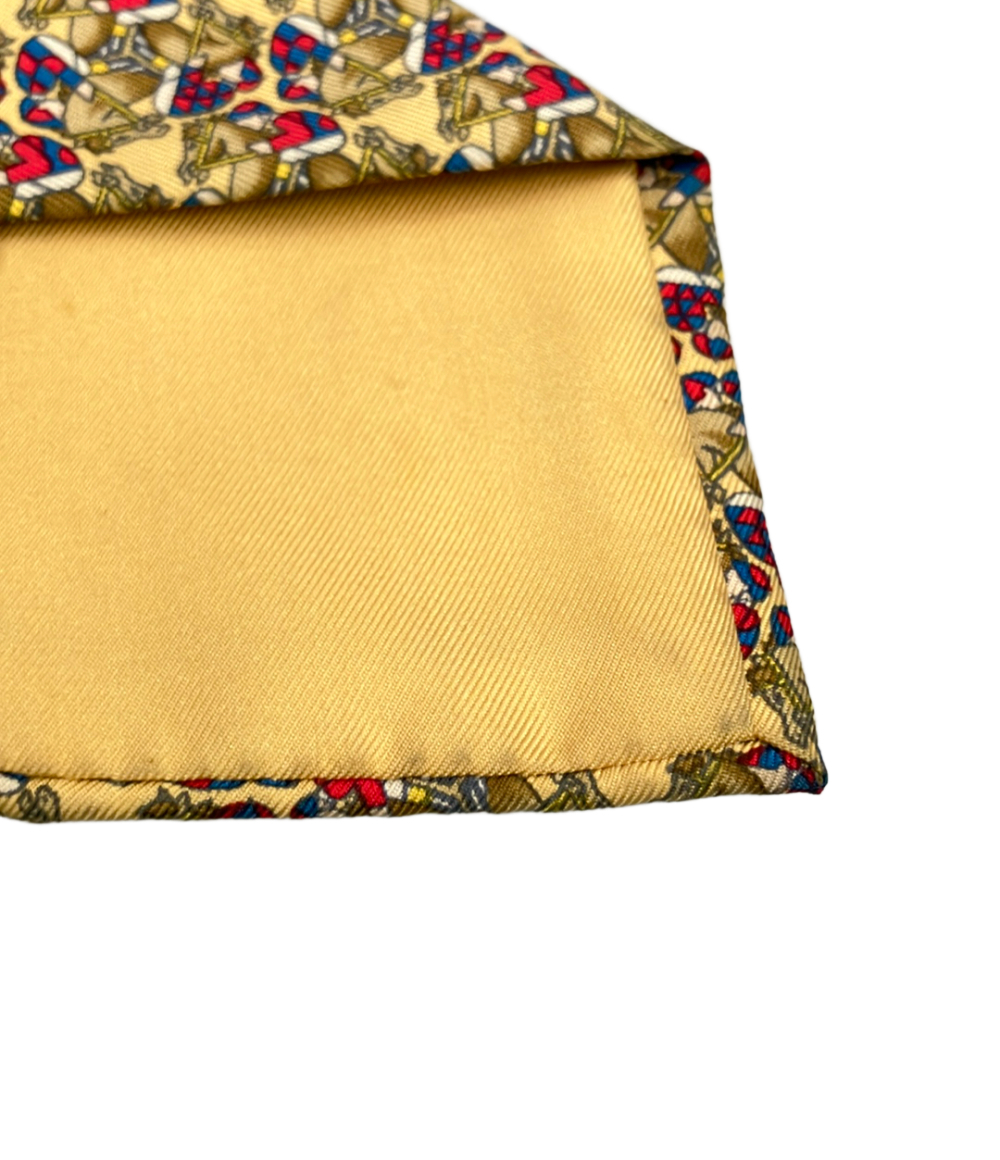 Cravatta Hermès in seta giallo paglia con cavalli e fantini in rosso e blu, ripiegata su fondo bianco — vista 5