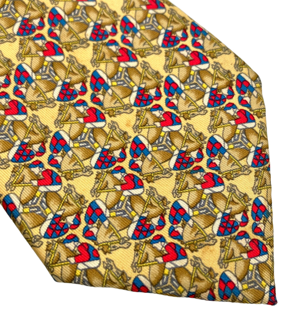 Cravatta Hermès in seta giallo paglia con cavalli e fantini in rosso e blu, ripiegata su fondo bianco — vista 6