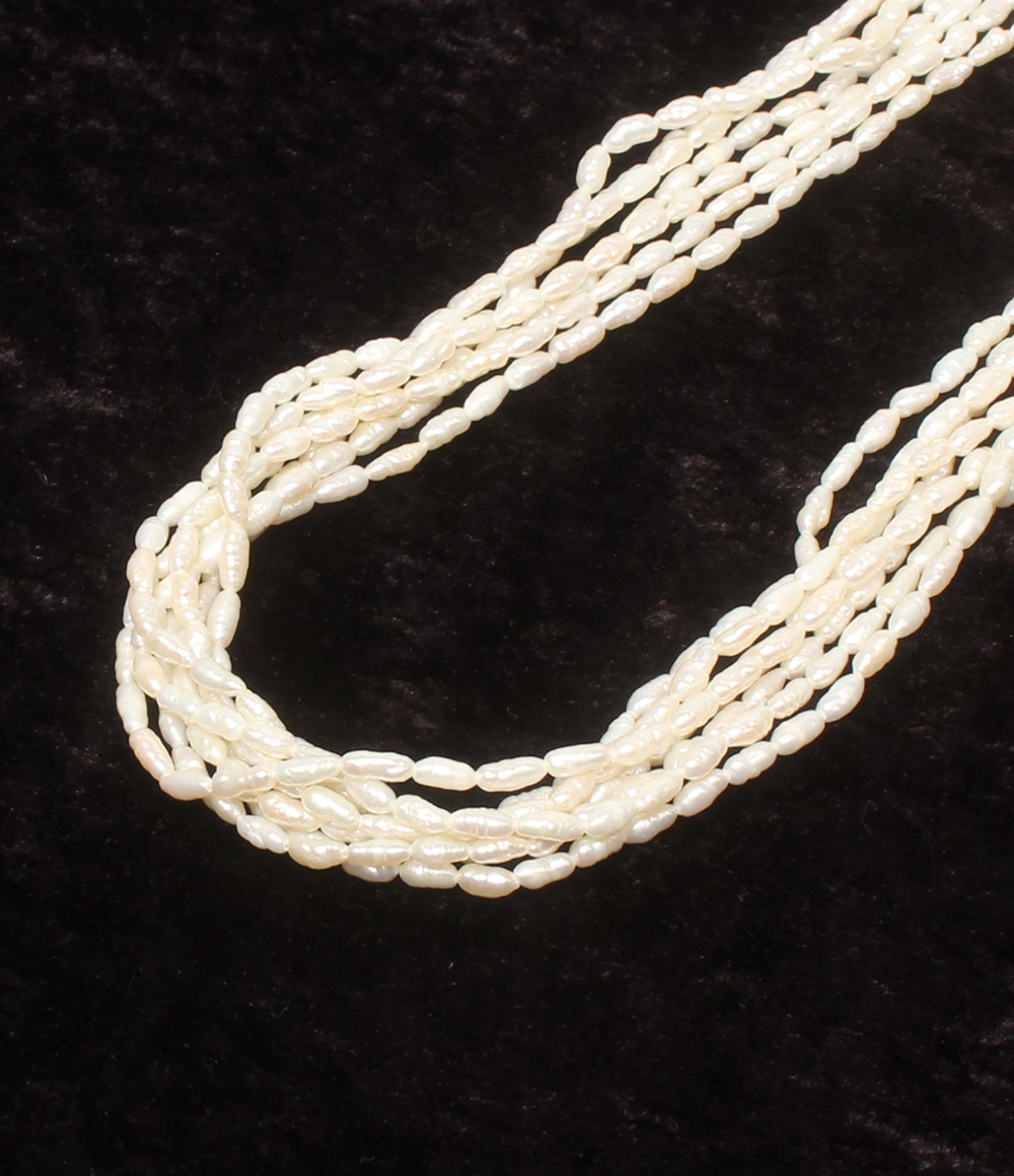 Collana a più fili di perline bianche a chicco di riso su velluto scuro, con fermaglio tondo lavorato a foglie color argento.