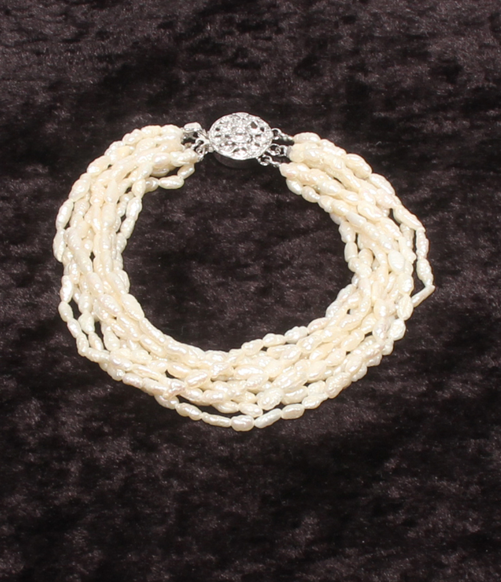 Bracciale a più fili di perline avorio a chicco di riso, con fermaglio rotondo traforato in argento, su velluto scuro.