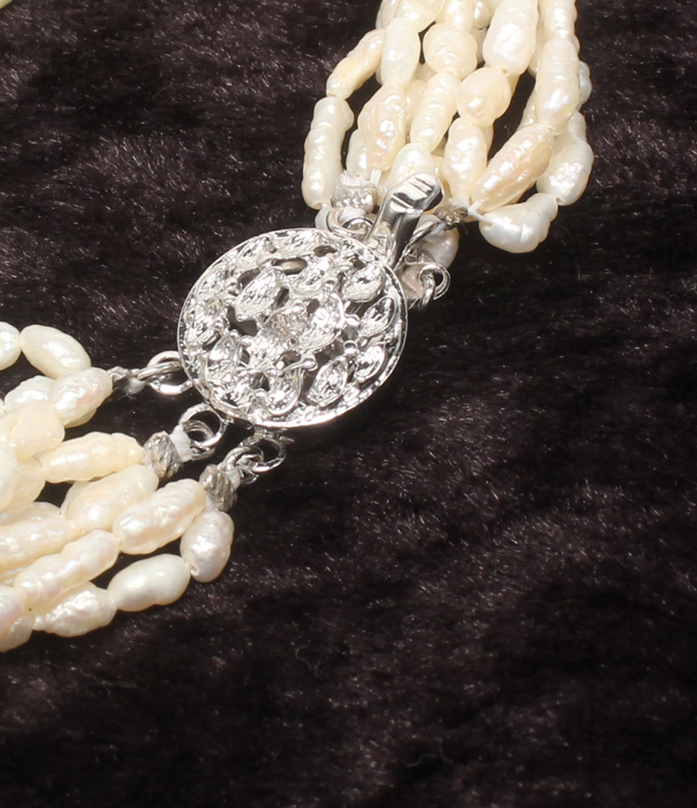 Bracciale a più fili di perline avorio a chicco di riso, con fermaglio rotondo traforato in argento, su velluto scuro. — vista 5