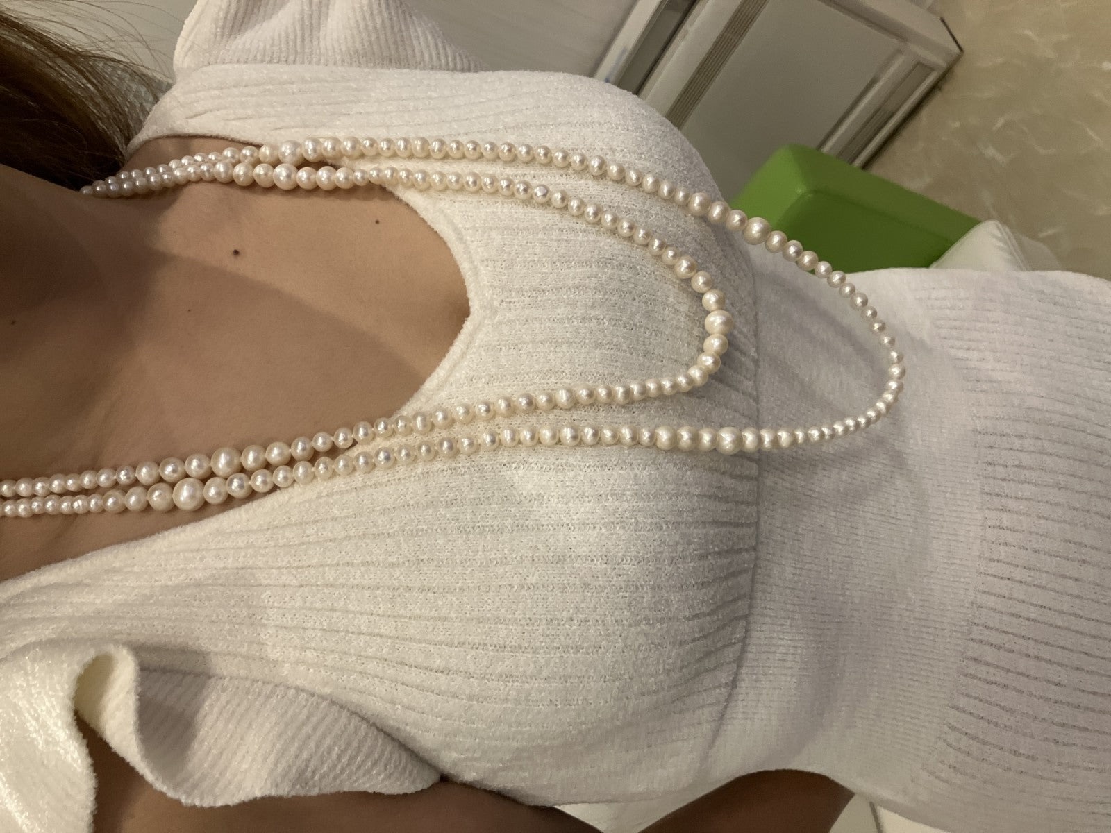 Collana lunga di perle bianche di misura alternata, indossata a doppio giro su un abito bianco a coste