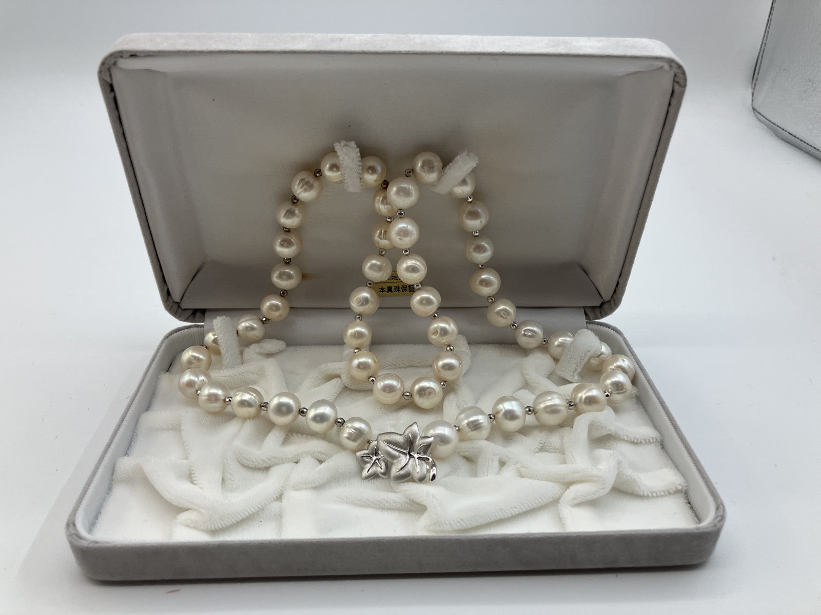 Collana di perle coltivate bianche con piccoli distanziatori argentati, indossata su un maglione rosa chiaro