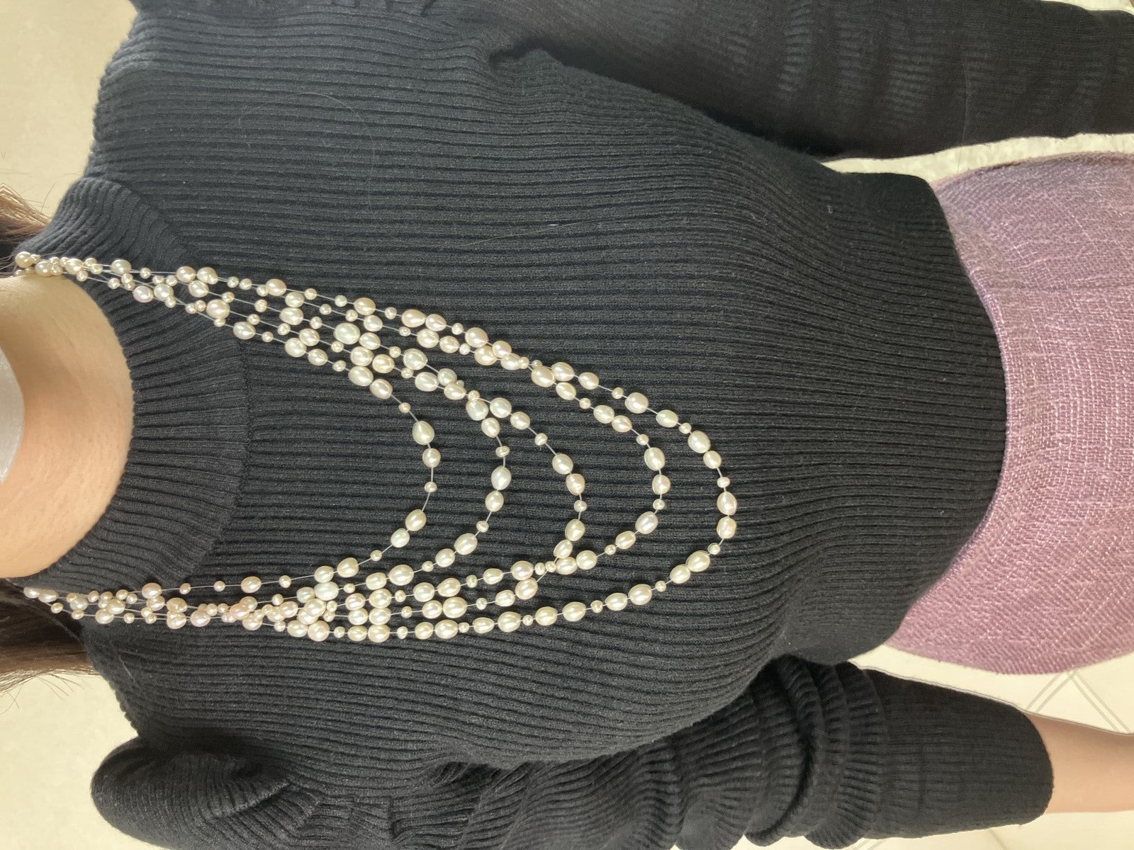 Collana a cinque fili di perle bianche d'acqua dolce su filo trasparente, a cascata, indossata su un maglione nero