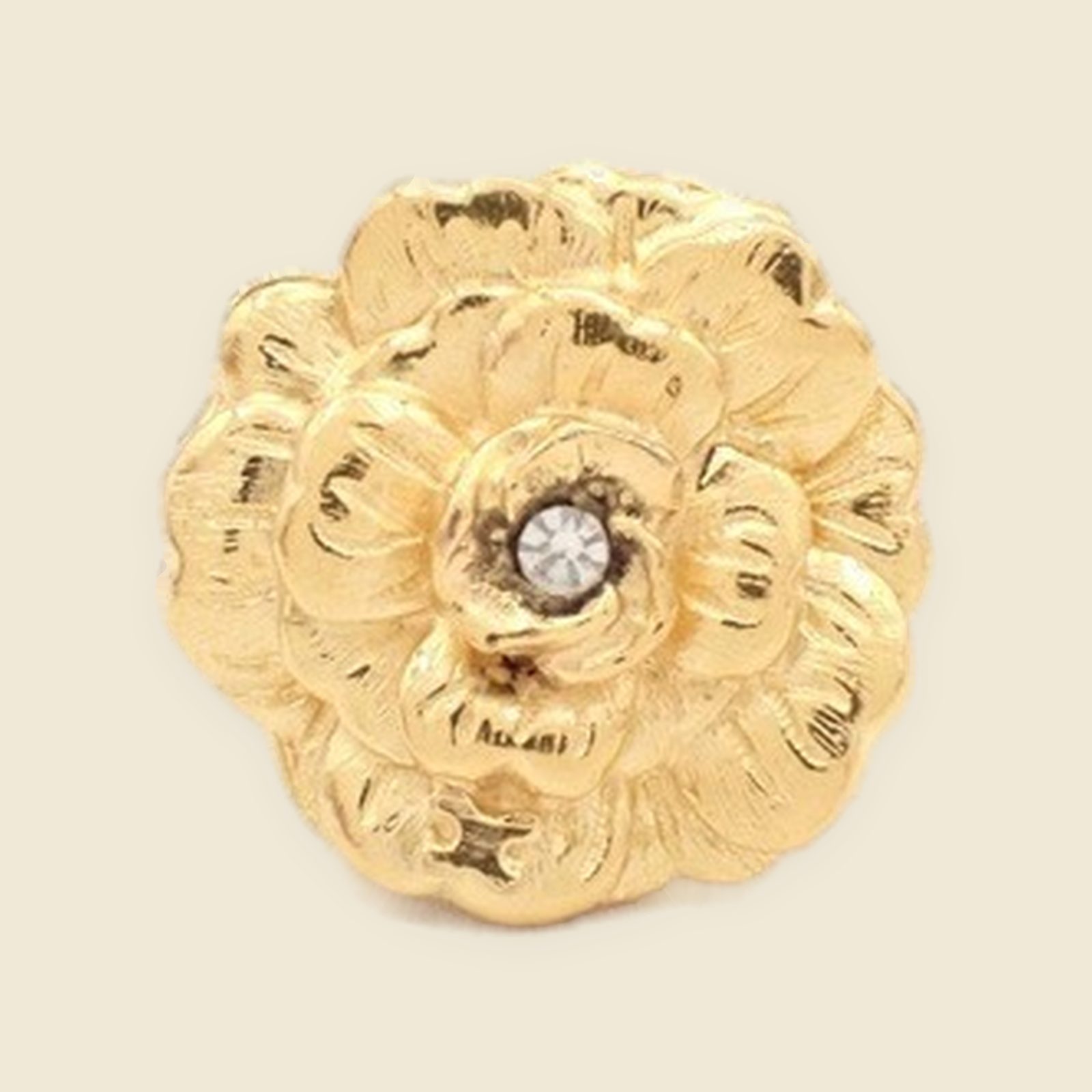 Orecchino a clip Chanel in metallo dorato a forma di fiore, con piccola pietra chiara al centro, su fondo bianco.