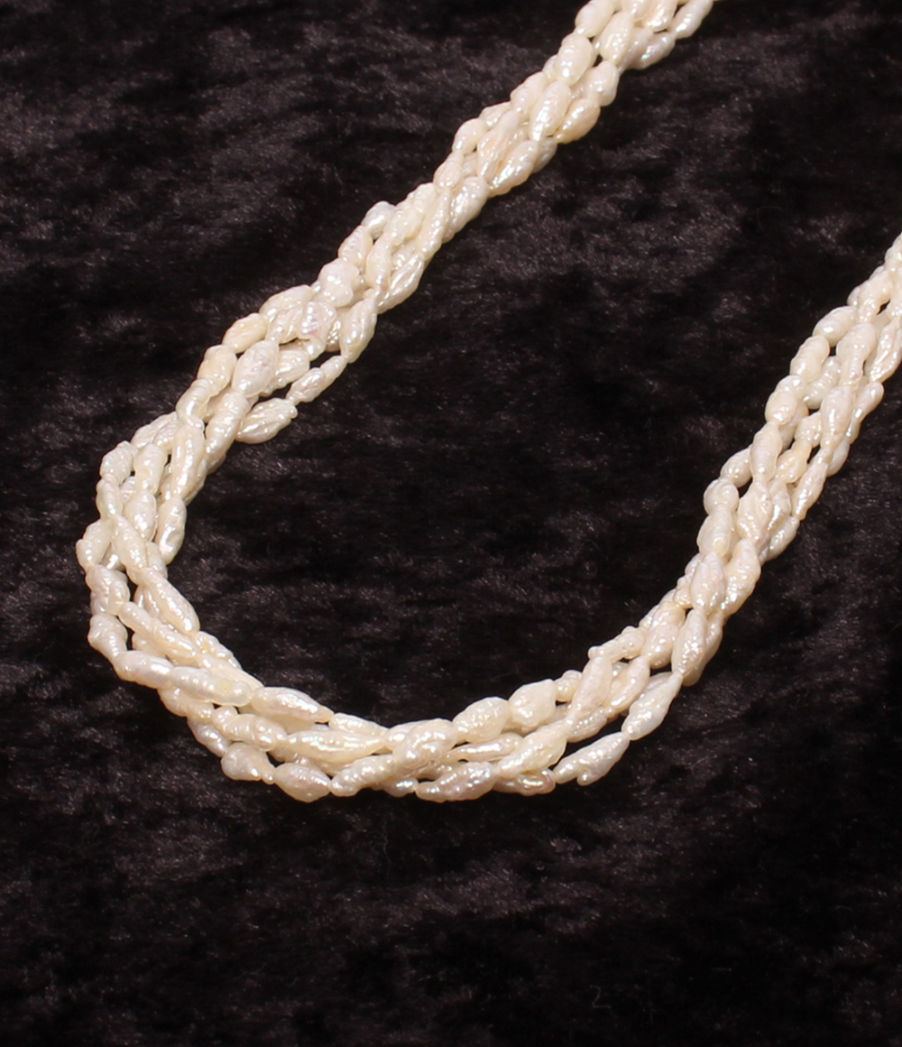 Collana a più fili di piccole perle bianche irregolari, intrecciati fra loro, posata su velluto scuro.
