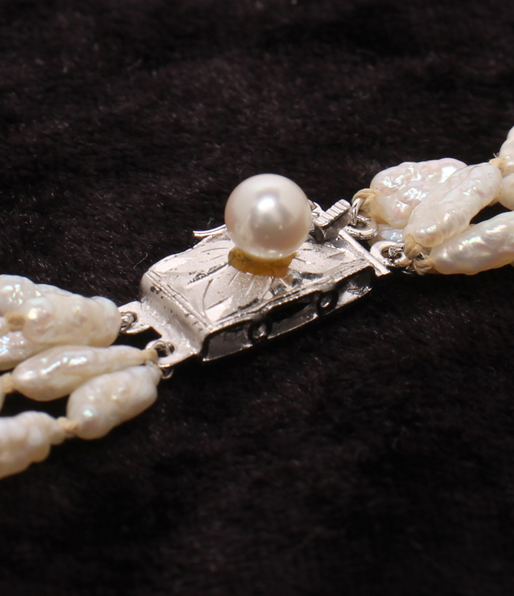 Collana a più fili di piccole perle bianche irregolari, intrecciati fra loro, posata su velluto scuro. — vista 5