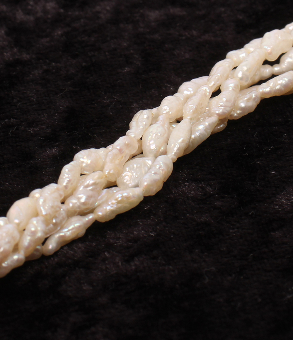Collana a più fili di piccole perle bianche irregolari, intrecciati fra loro, posata su velluto scuro. — vista 7