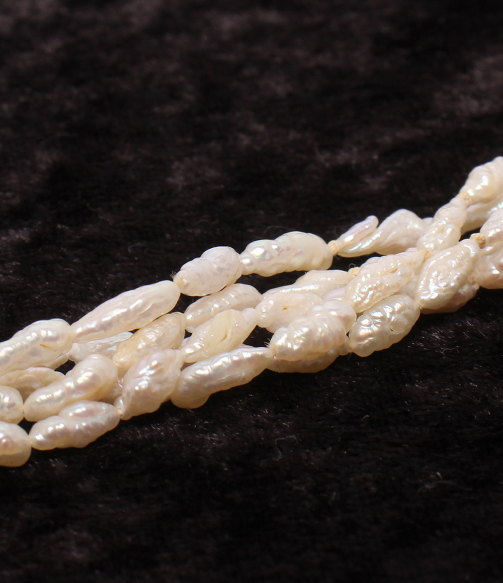 Collana a più fili di piccole perle bianche irregolari, intrecciati fra loro, posata su velluto scuro. — vista 8