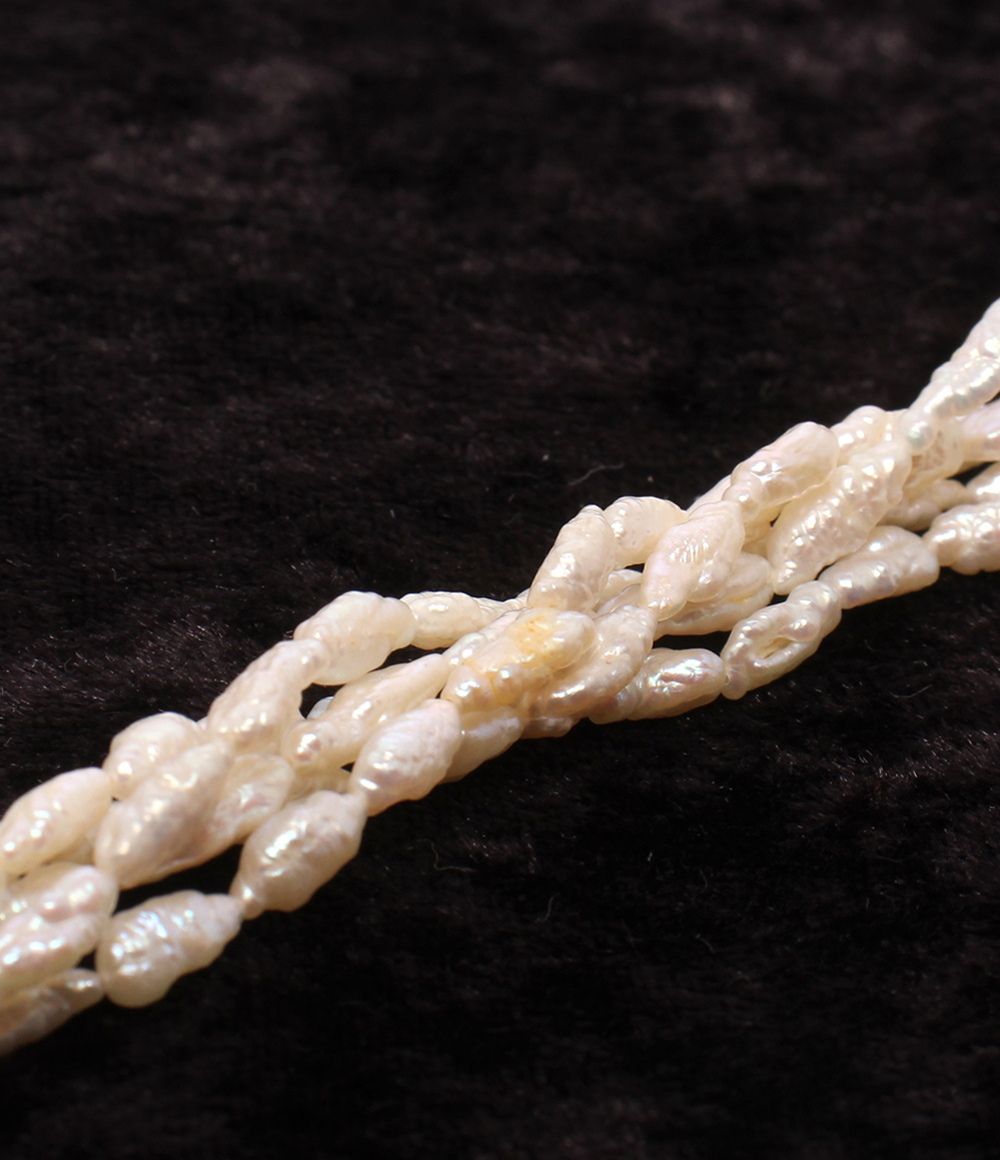 Collana a più fili di piccole perle bianche irregolari, intrecciati fra loro, posata su velluto scuro. — vista 9